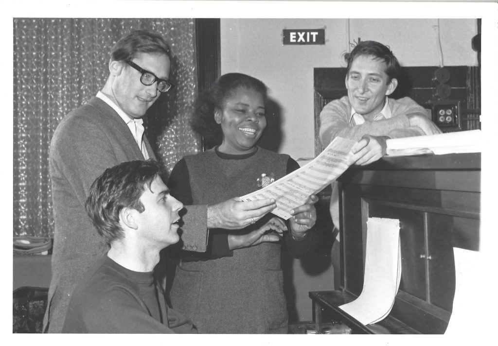 A black and white photo of four people reading a script.
